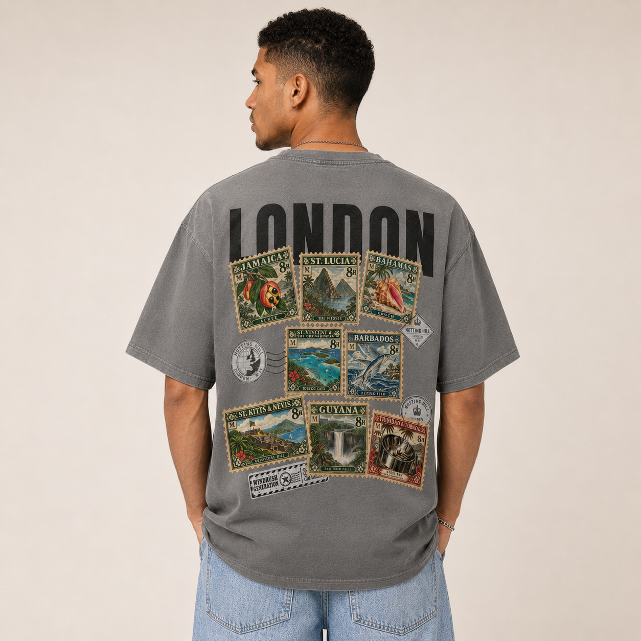 A man seen from behind wearing the mid-grey Maknesan tee with wide light denim, black LONDON wordmark above the Caribbean stamp collage.